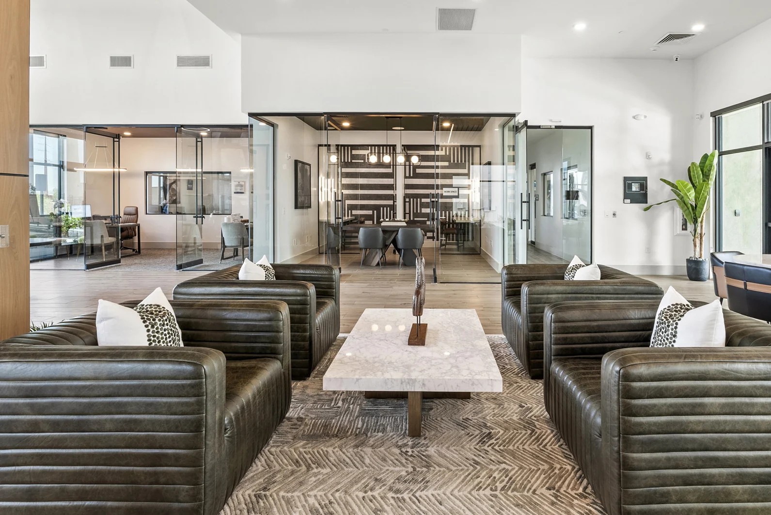 The finished lobby and lounge, photographed: channel-tufted leather chairs around a marble coffee table, the glass-walled meeting room beyond